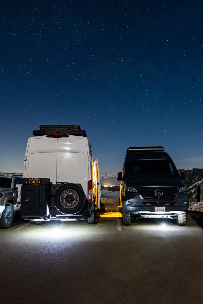 Two camper vans parked under a clear, starry night sky, perfect for a road trip.
